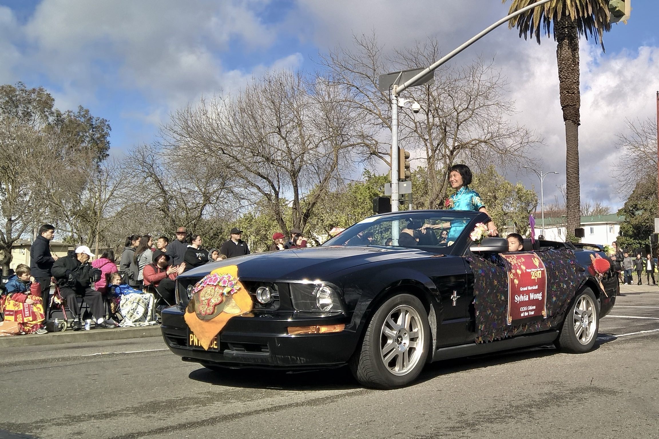 Sylvia Wong, the Grand Marshall of the Stockton Chinese New Year parade and CCSS Citizen of the Year, smiles as she stands inside a black Ford Mustang convertible.