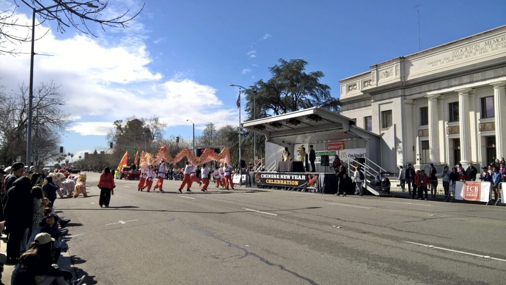 The volunteers from the Concord Kung Fu Academy dance in a circle while holding a dragon in front of a stage set up in front of the Stockton Memorial Civic Center. A sign in front of the stage reads Chinese New Year Celebration.