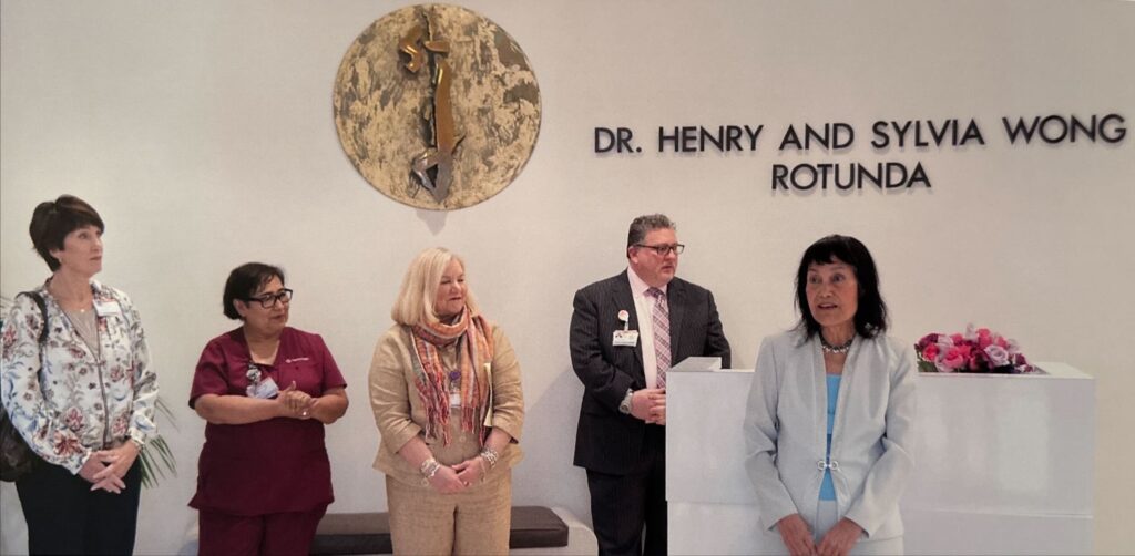 Sylvia Wong speaking to the audience at the Dr. Henry and Sylvia Wong Rotunda, with four staff members of St. Joseph's Medical Center behind her